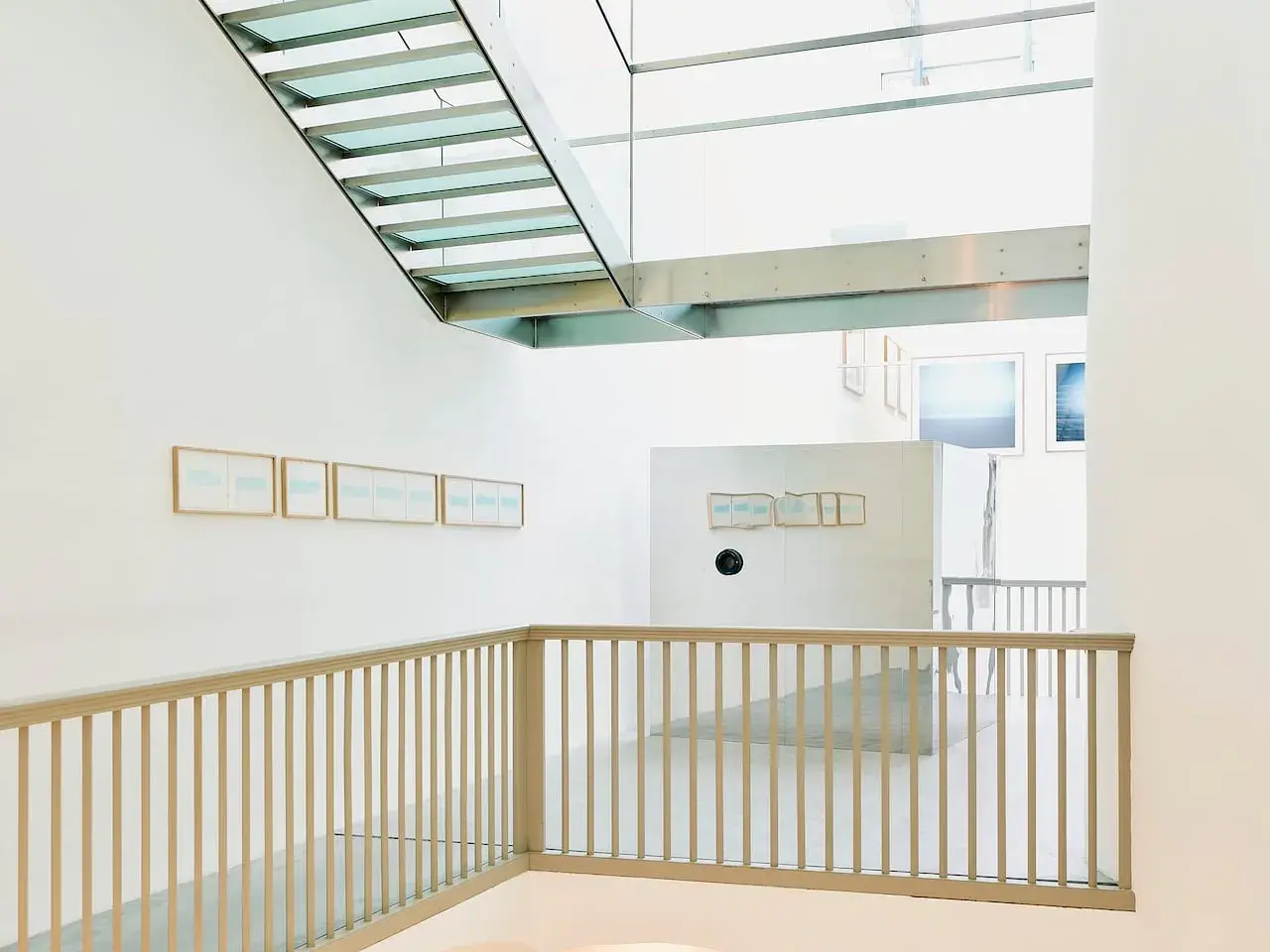 Interno moderno con scale in vetro e metallo. Opere di Christian Martinelli appese alle pareti bianche.