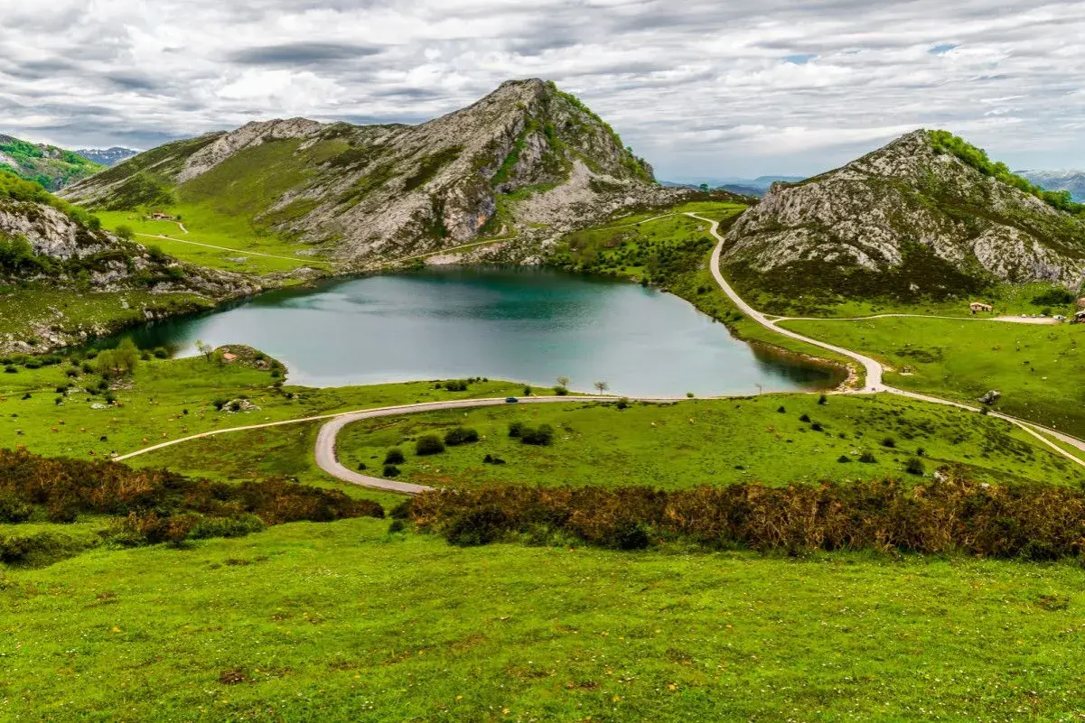 Un lago sereno rodeado de verdes colinas y picos rocosos, un paisaje idílico para ver Picos de Europa.