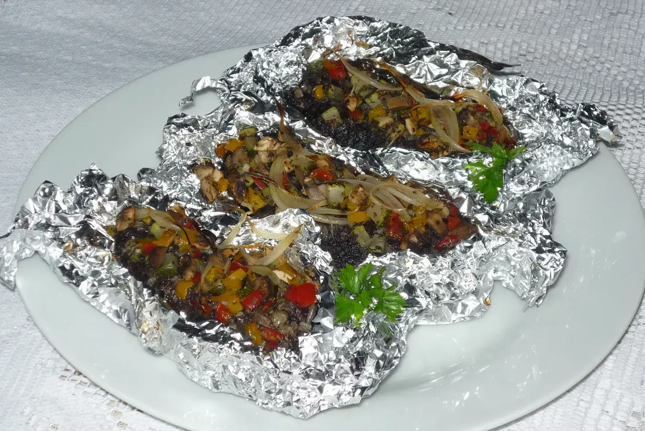 Kaszanka z grilla z cebulą i warzywami, zapieczona w folii aluminiowej, podana na białym talerzu.