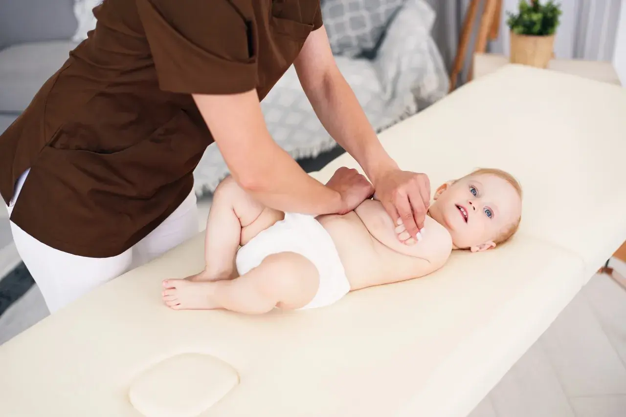 Niemowlę na masażu. Terapeuta wykonuje ćwiczenia metodą Vojty, stymulując rozwój dziecka.
