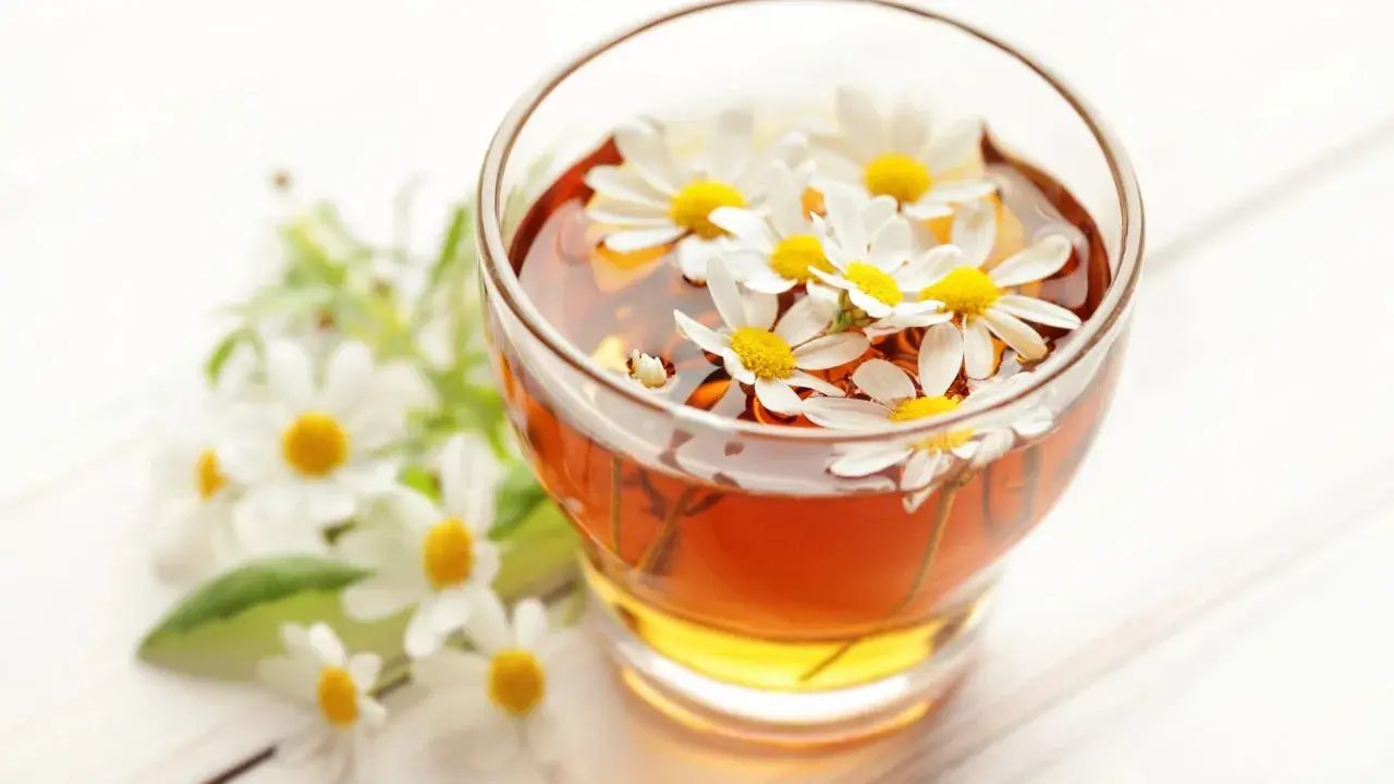 Un bicchiere di camomilla per bambini, con fiori freschi che galleggiano nella bevanda dorata.