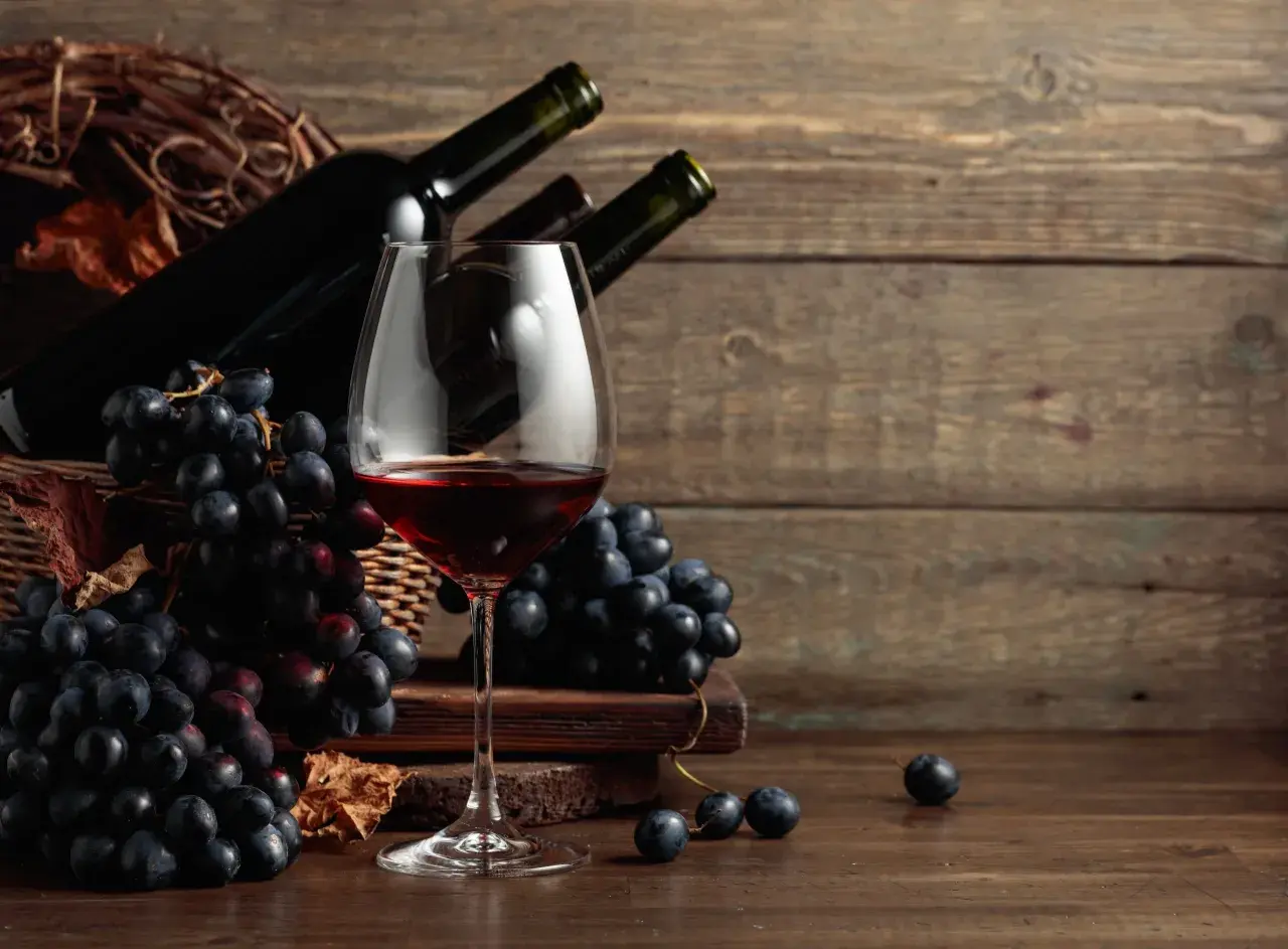 Calice di vino rosso, grappoli d'uva nera e bottiglie in un cesto. Ideale per scoprire i migliori sassicaia abbinamenti.