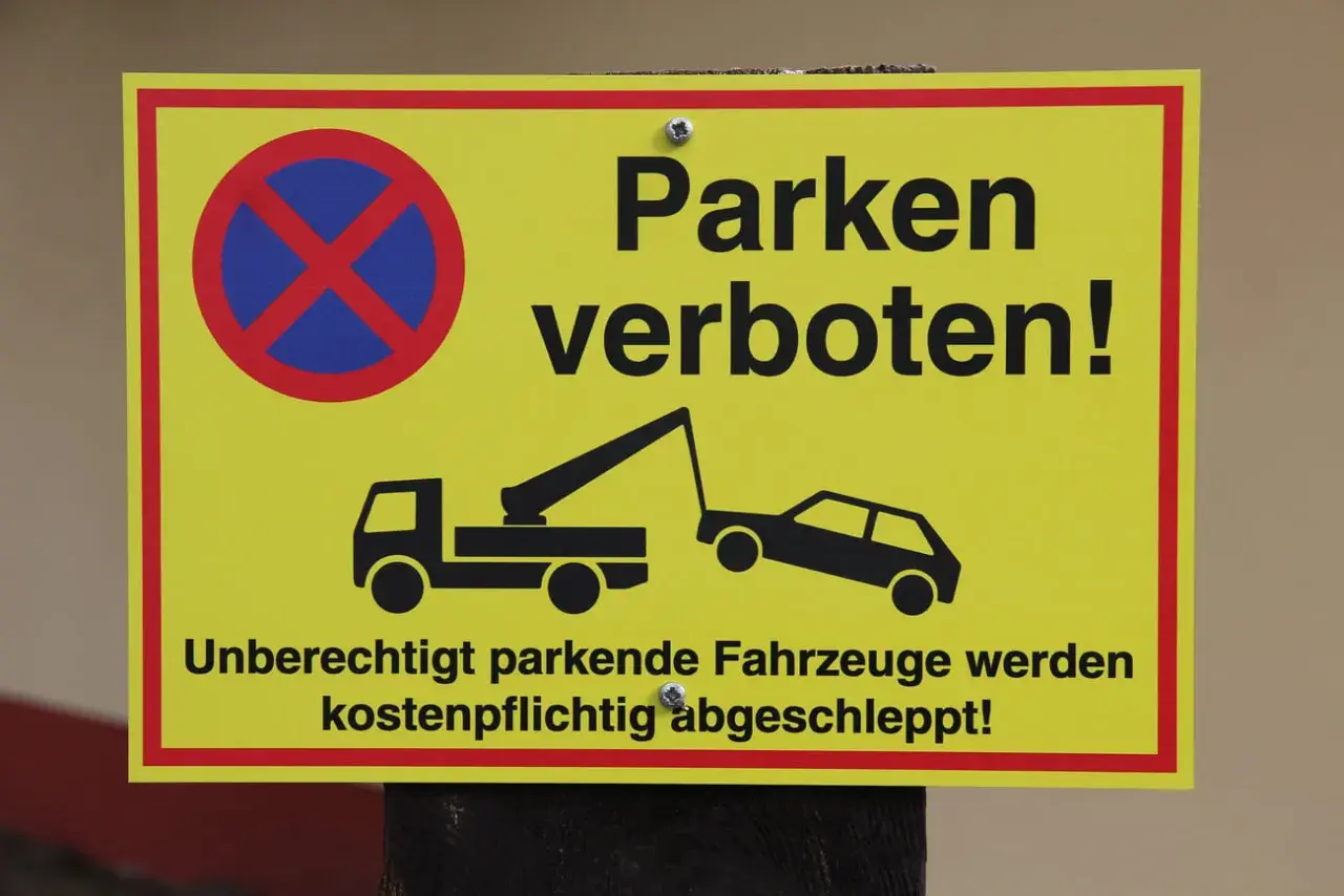 Gelbes Schild: Parken verboten! Ein Abschleppwagen holt ein schlecht geparktes Auto ab. Unberechtigt parkende Fahrzeuge werden kostenpflichtig abgeschleppt!