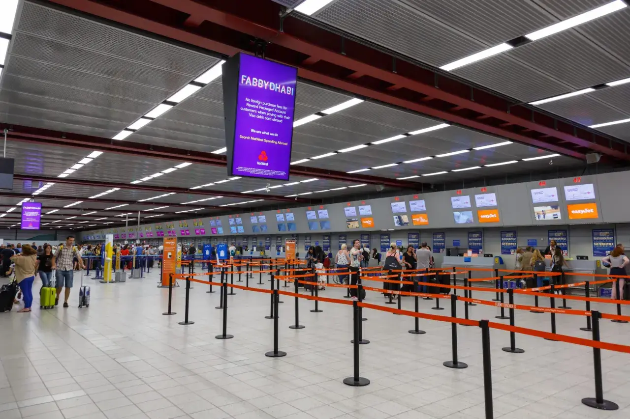 Kasa odpraw na lotnisku Londyn Luton. Pasażerowie z bagażami czekają w kolejce do stanowisk linii lotniczych easyJet.