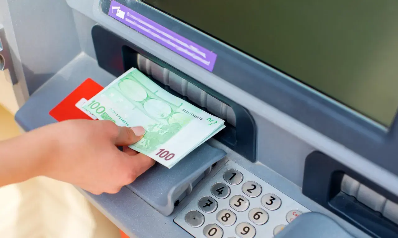 Ręka odbiera banknoty 100 euro z bankomatu PKO.