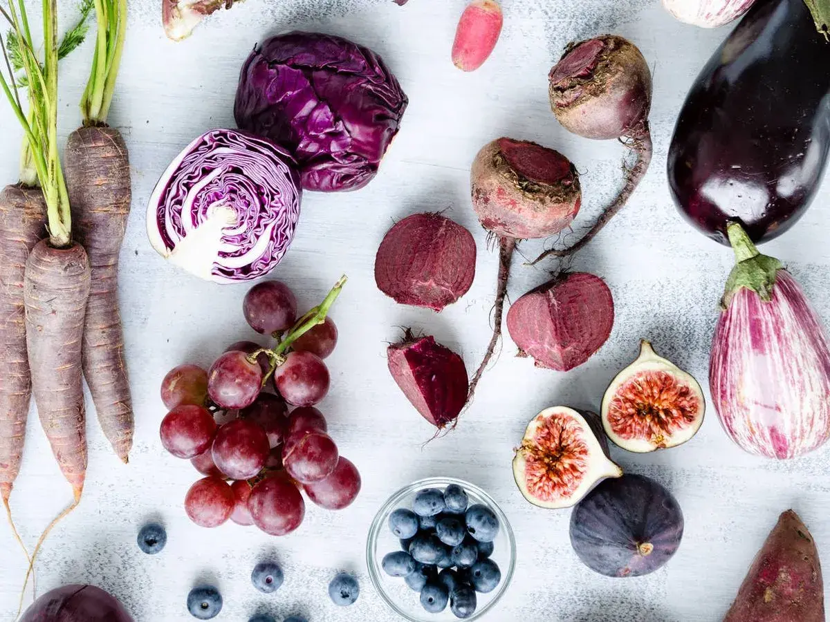 Un surtido de verduras raras y frutas moradas: zanahorias, col lombarda, remolachas, berenjenas, higos, uvas y arándanos.