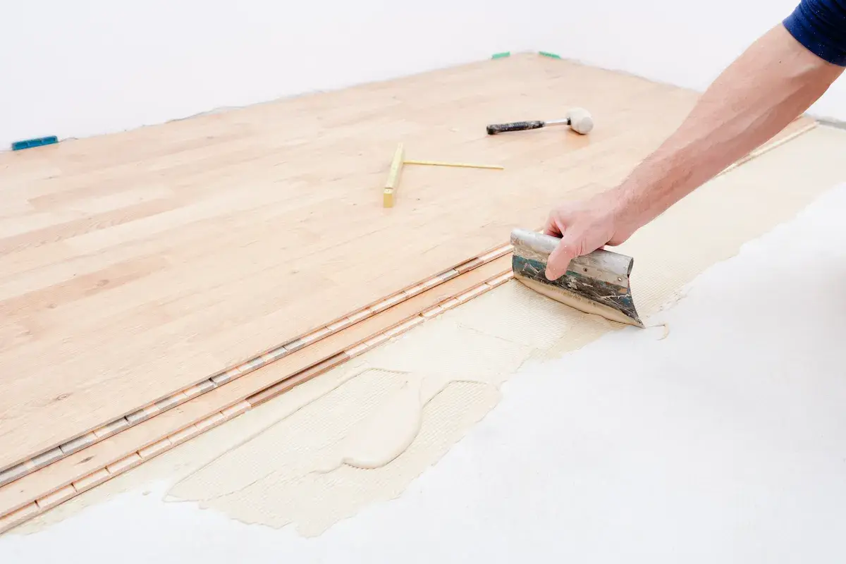 Pose d'un plancher bois étage : application de colle avec une spatule sur le support avant la pose des lames.
