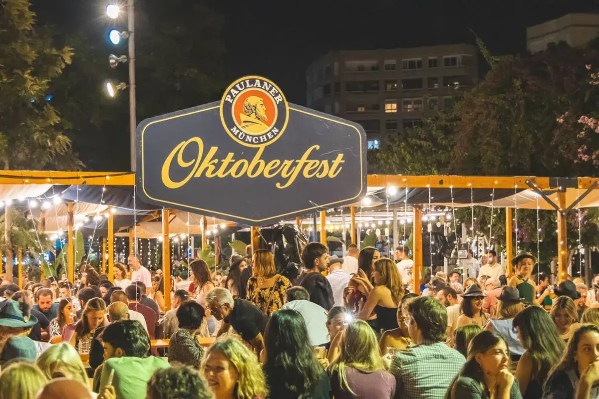 Gente disfrutando en un evento de Oktoberfest Valencia, con luces y un gran cartel de Paulaner.