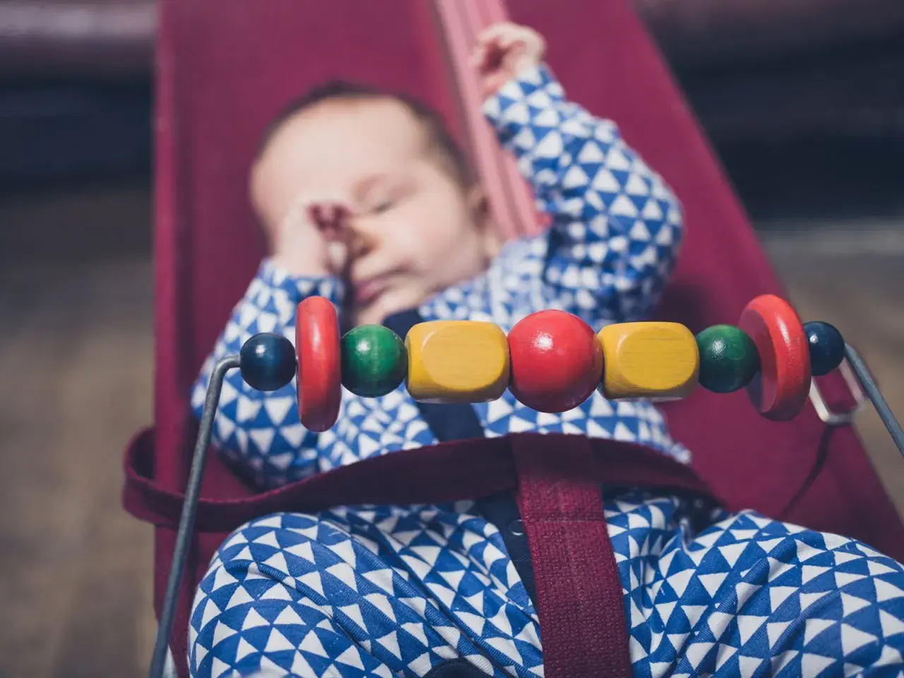 Sover gott i sin babysitter elektrisk, med färgglada träpärlor som leksak.