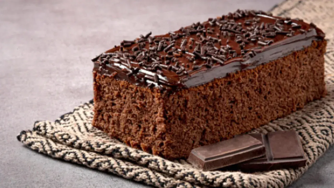 Un delicioso pastel de chocolate cubierto con glaseado y chispas de chocolate, acompañado de trozos de chocolate.