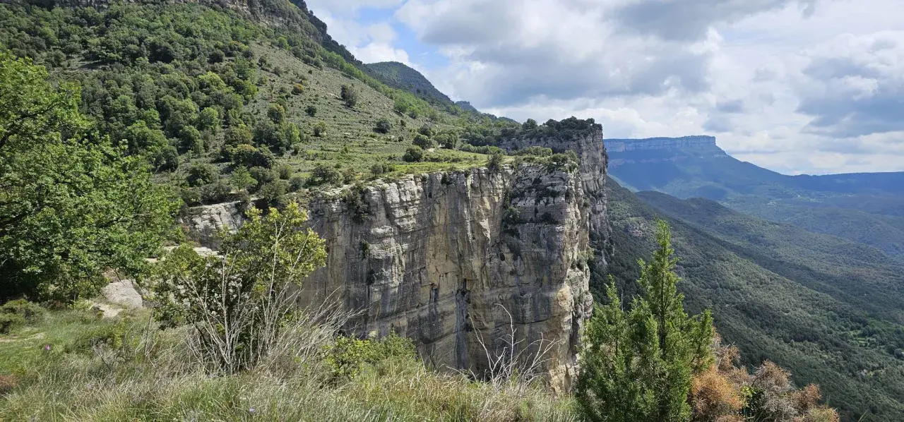 Impresionante pared rocosa del salt de sallent, con vegetación verde y un cielo nublado.