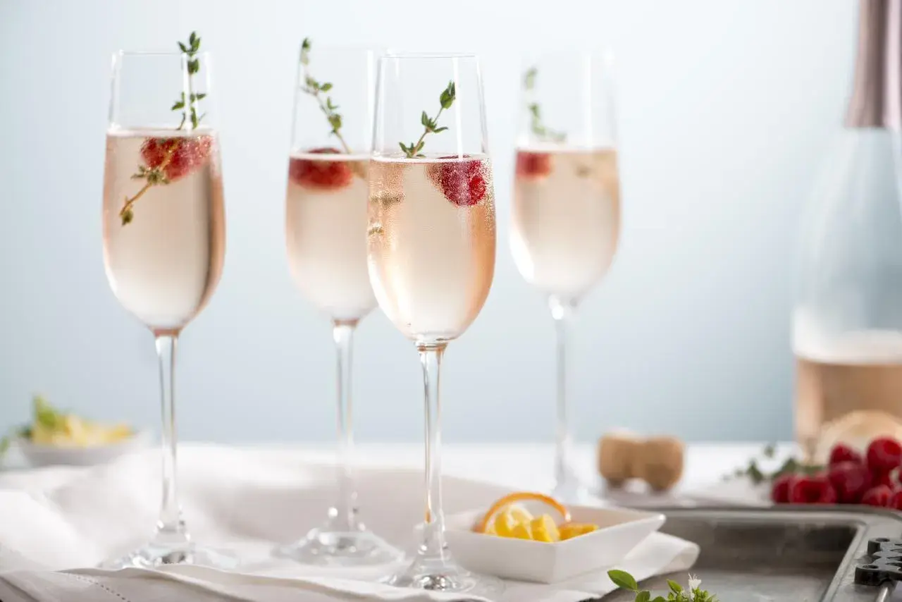 Quatre flûtes de soupe de champagne rosée, garnies de framboises et de thym, prêtes à être dégustées.