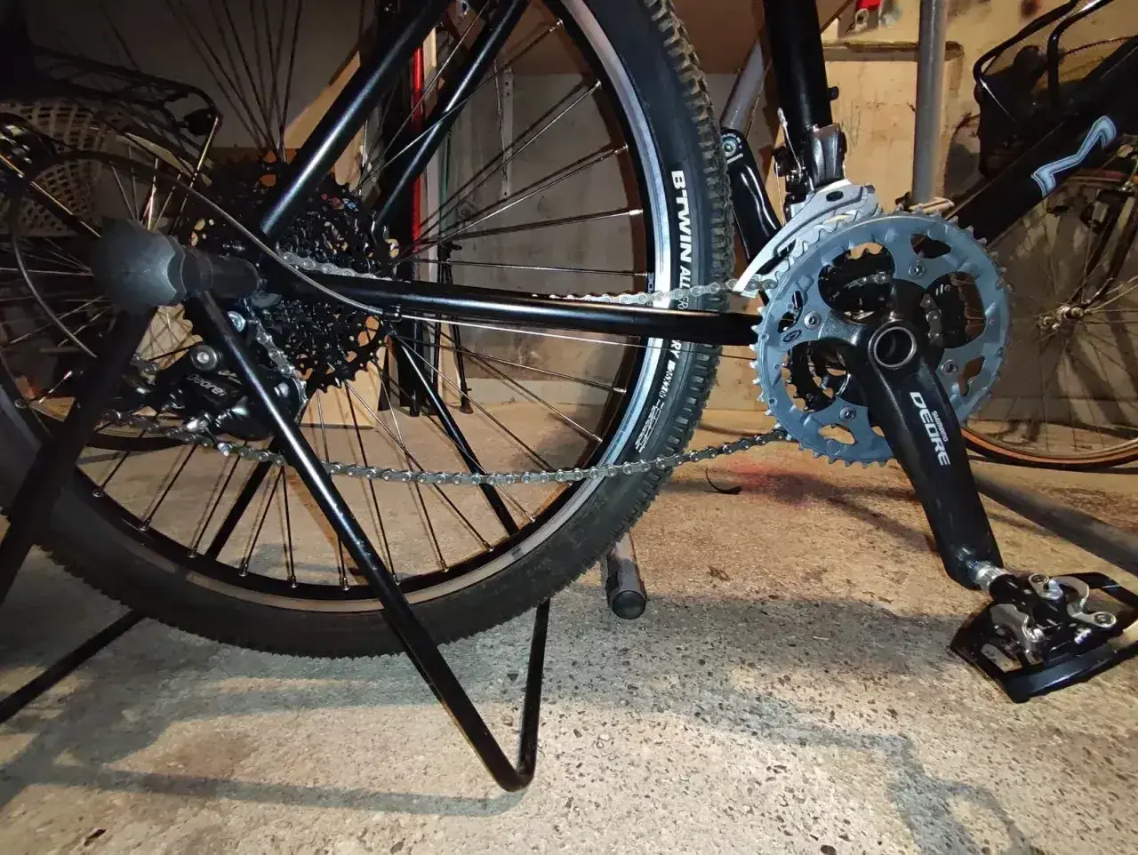 Widok tylnego koła i korby roweru. Pokazuje mechanizm przerzutek i łańcuch, który można naciągnąć, aby rower działał płynnie.