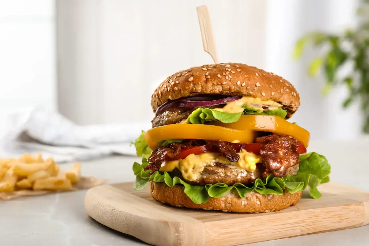 Un délicieux hamburger au barbecue, garni de bacon croustillant, de fromage fondant et de légumes frais, servi sur une planche en bois.