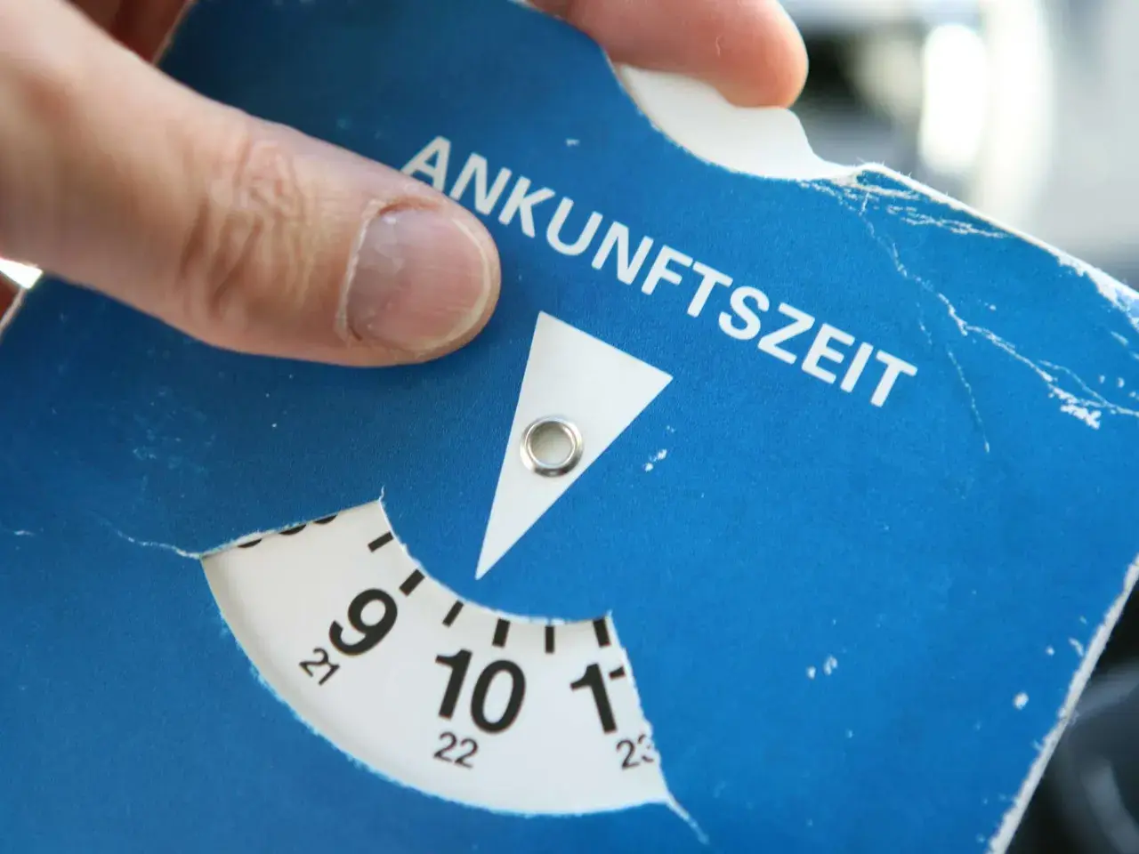 Ein Finger dreht die Scheibe einer Parkscheibe, um die Ankunftszeit einzustellen. So funktioniert eine Parkuhr: Zeit einstellen, auslegen, fertig.