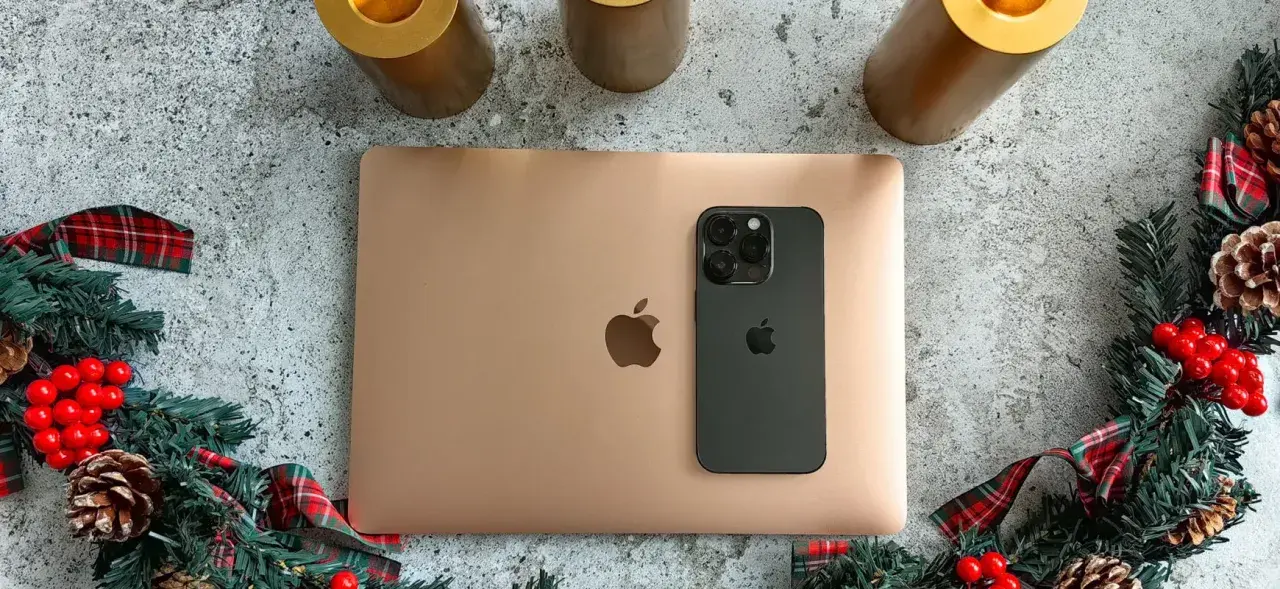 Złoty MacBook i czarny iPhone na tle świątecznych dekoracji. Idealny zestaw do pracy i rozrywki z macOS.