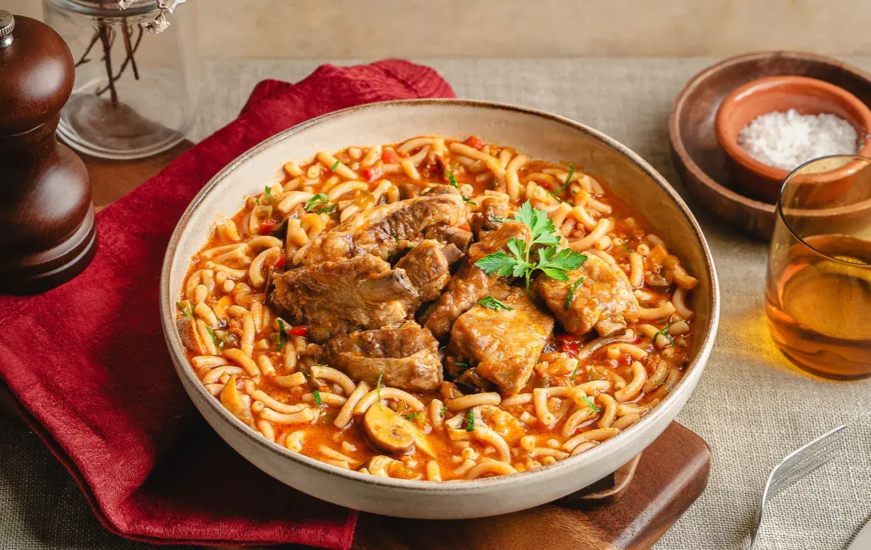 Un reconfortante plato de fideos a la cazuela con costilla, servido en un cuenco rústico, con un toque de perejil fresco.