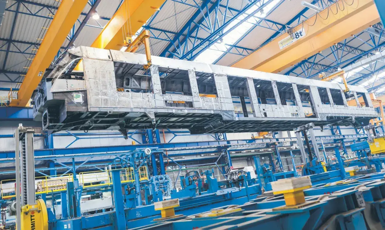 Szkielet wagonu kolejowego w hali produkcyjnej Alstom Chorzów, unoszony przez suwnicę.