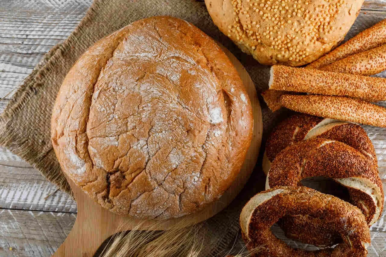 Różne rodzaje pieczywa: bochenek, paluszki sezamowe, obwarzanki i chleb z ziarnami.