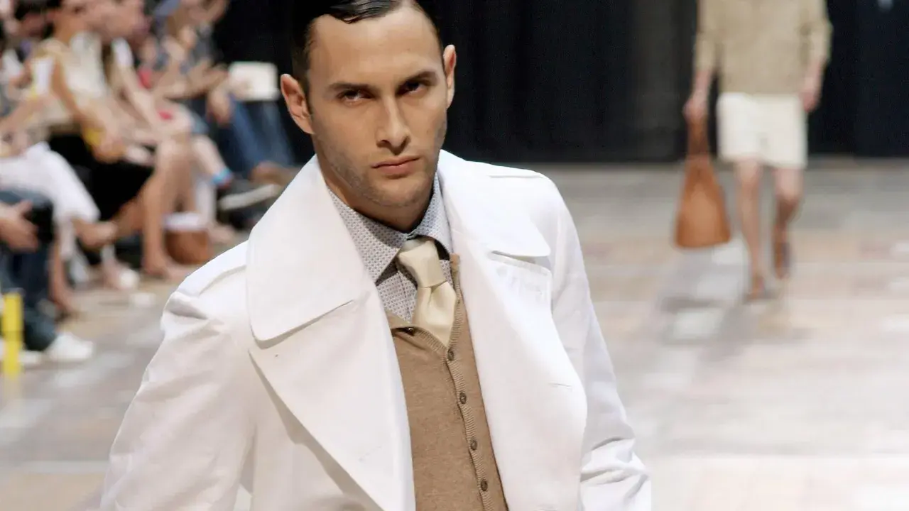 Ein Mann auf dem Laufsteg trägt einen weißen Trenchcoat über einem beigen Sakko, das er elegant kombiniert.