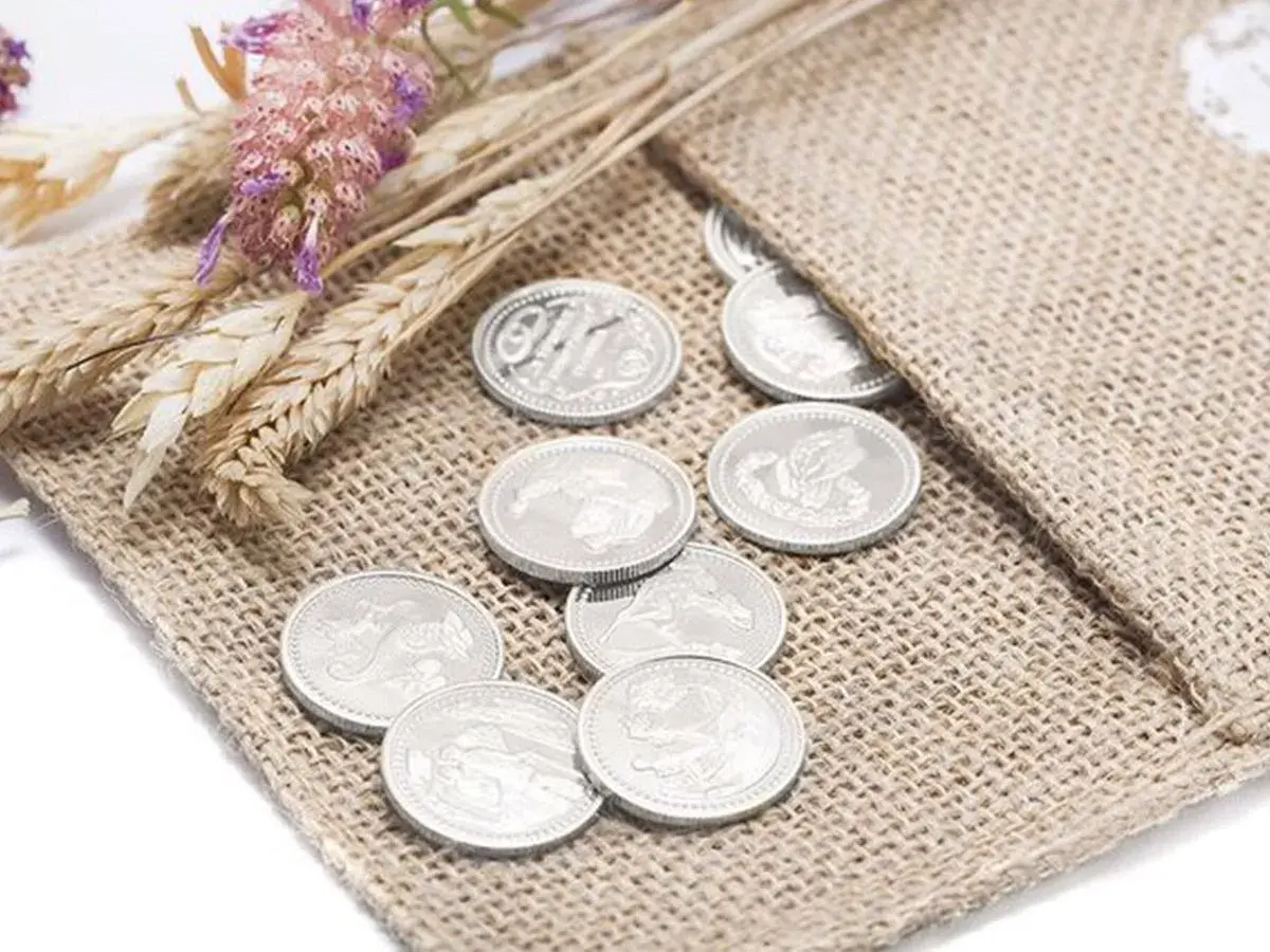 Monedas plateadas, símbolo de prosperidad, junto a espigas y flores secas, representando las arras de boda.