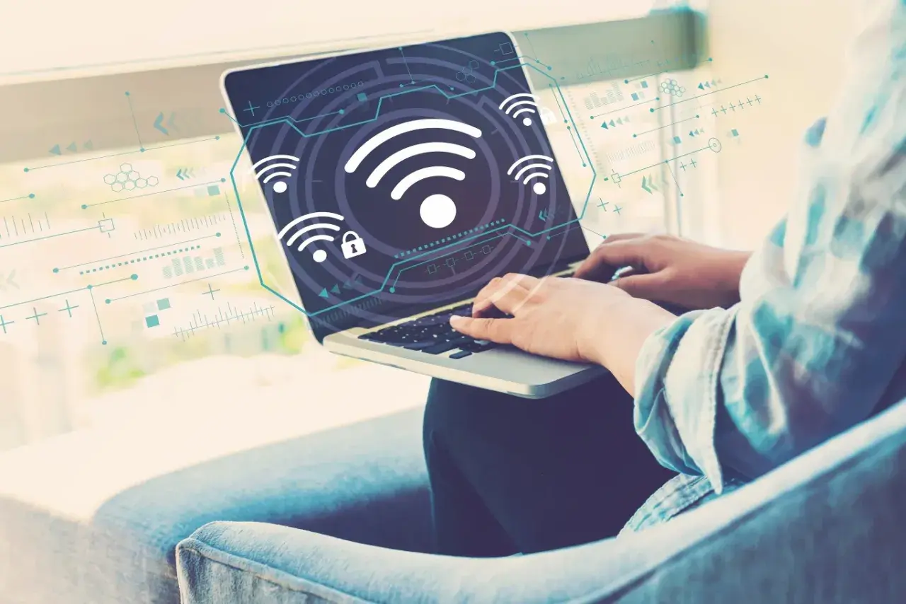 Osoba pracuje na laptopie, na ekranie widoczne są ikony Wi-Fi i schematy. Dowiedz się, jak włączyć Wi-Fi w laptopie.