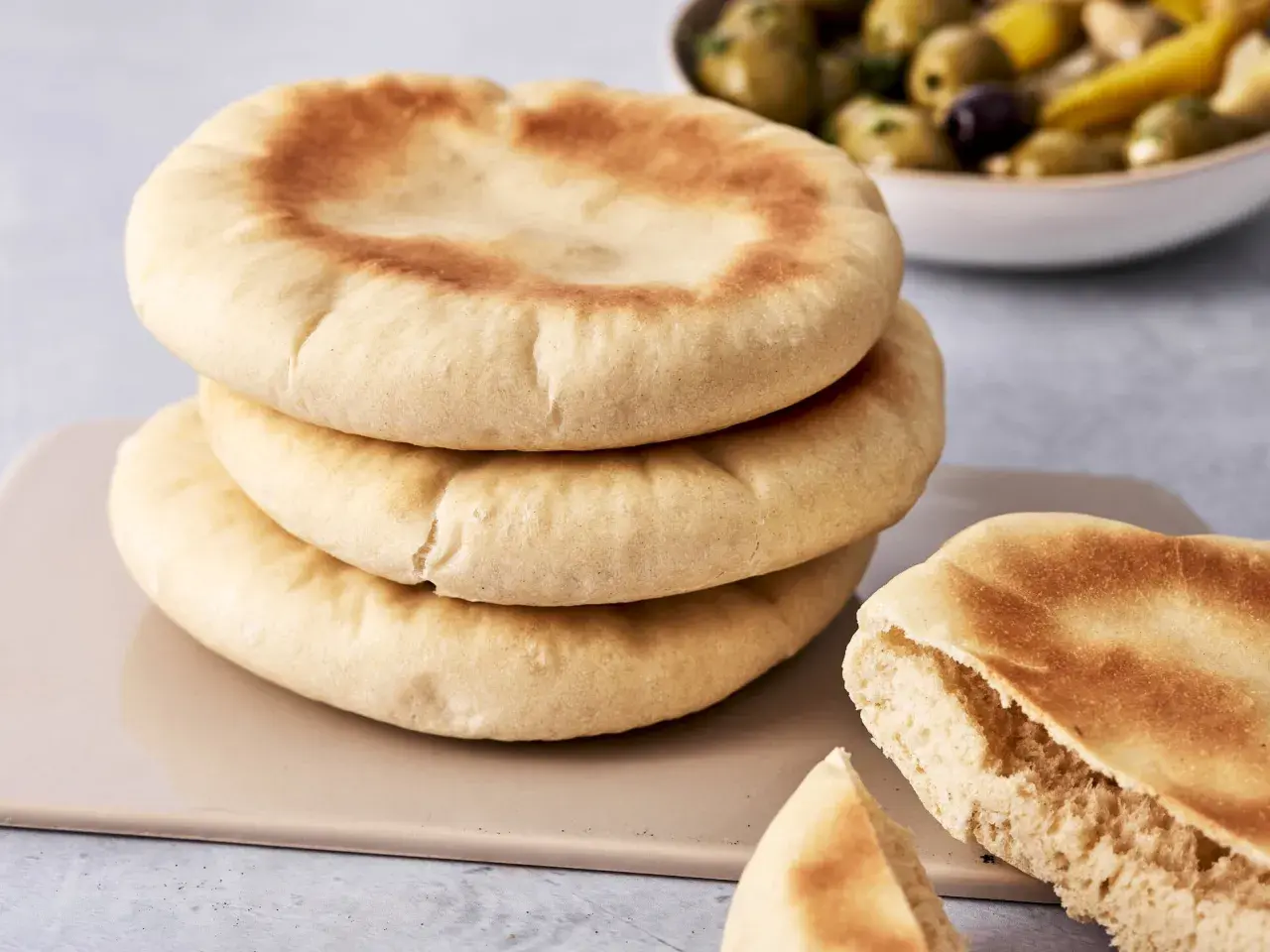 Gestapeltes pita brot mit einer Schüssel Oliven im Hintergrund. Ein Stück ist aufgeschnitten und zeigt die weiche Krume.