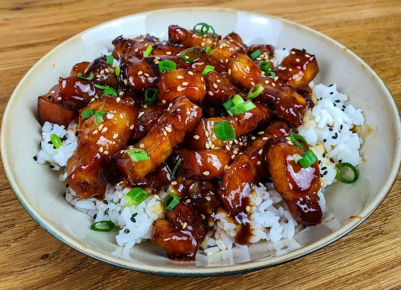 Un plat appétissant de porc au caramel asiatique, garni de graines de sésame et d'oignons verts, servi sur du riz blanc. Une recette à essayer !
