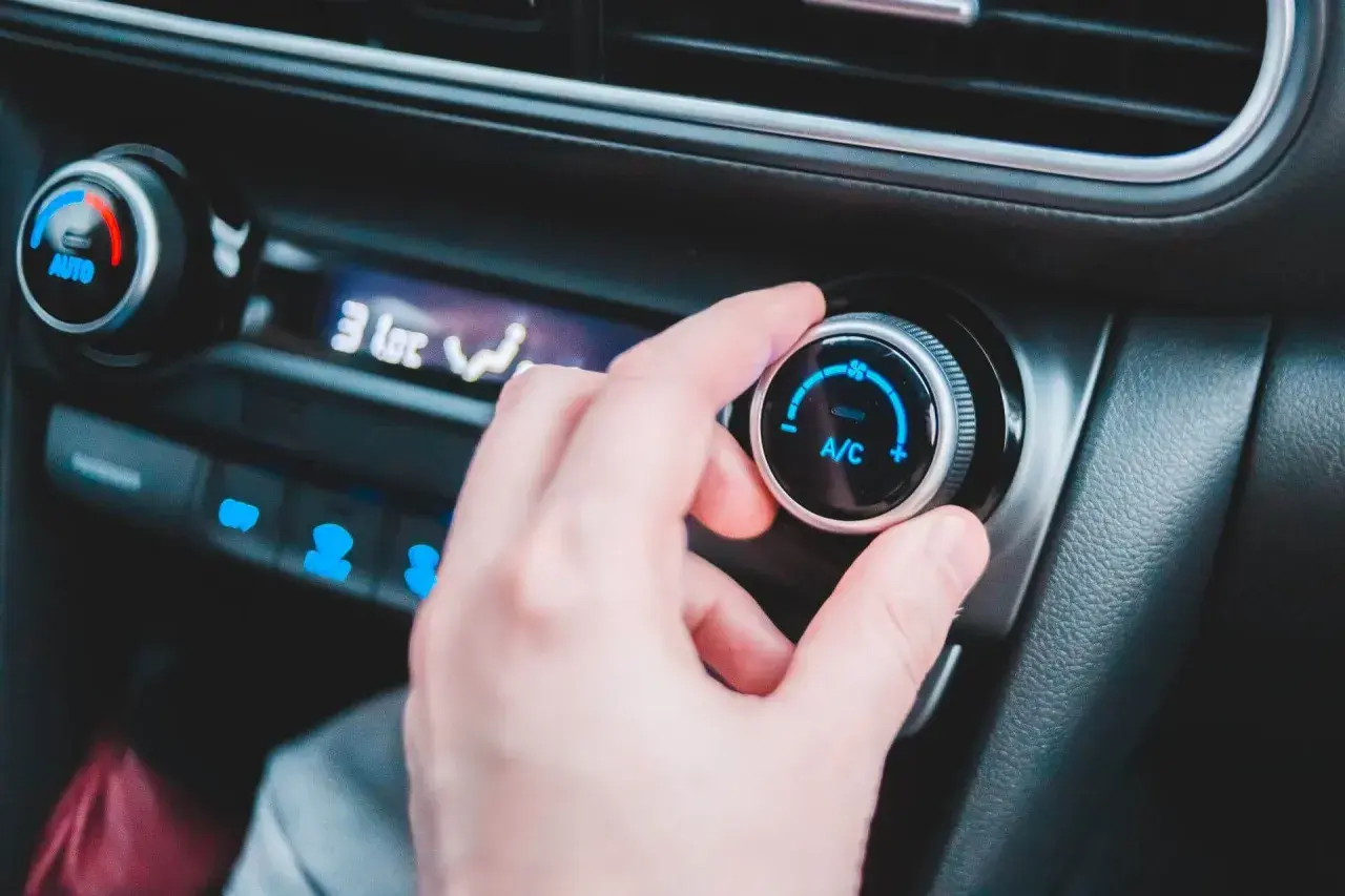 En hand vrider på reglaget för ac i bilen. Temperaturen sjunker snabbt.