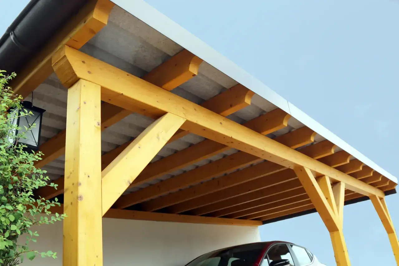 Holzkonstruktion eines Carports mit Trapezblechdach. Das Dach ist gut abgedichtet und schützt das darunter geparkte Auto.