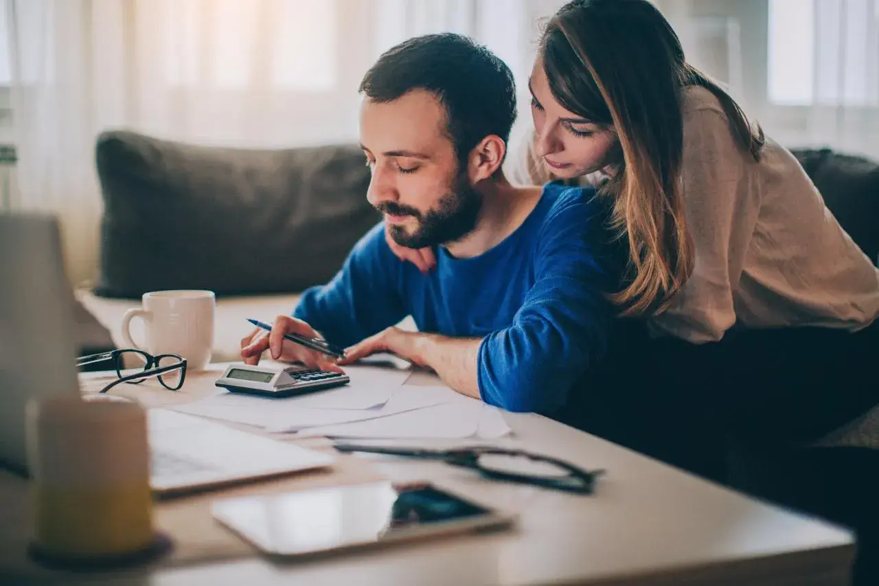 Ein Paar plant den Hausverkauf und fragt sich, wer die Notarkosten trägt. Sie sitzen am Tisch und rechnen.