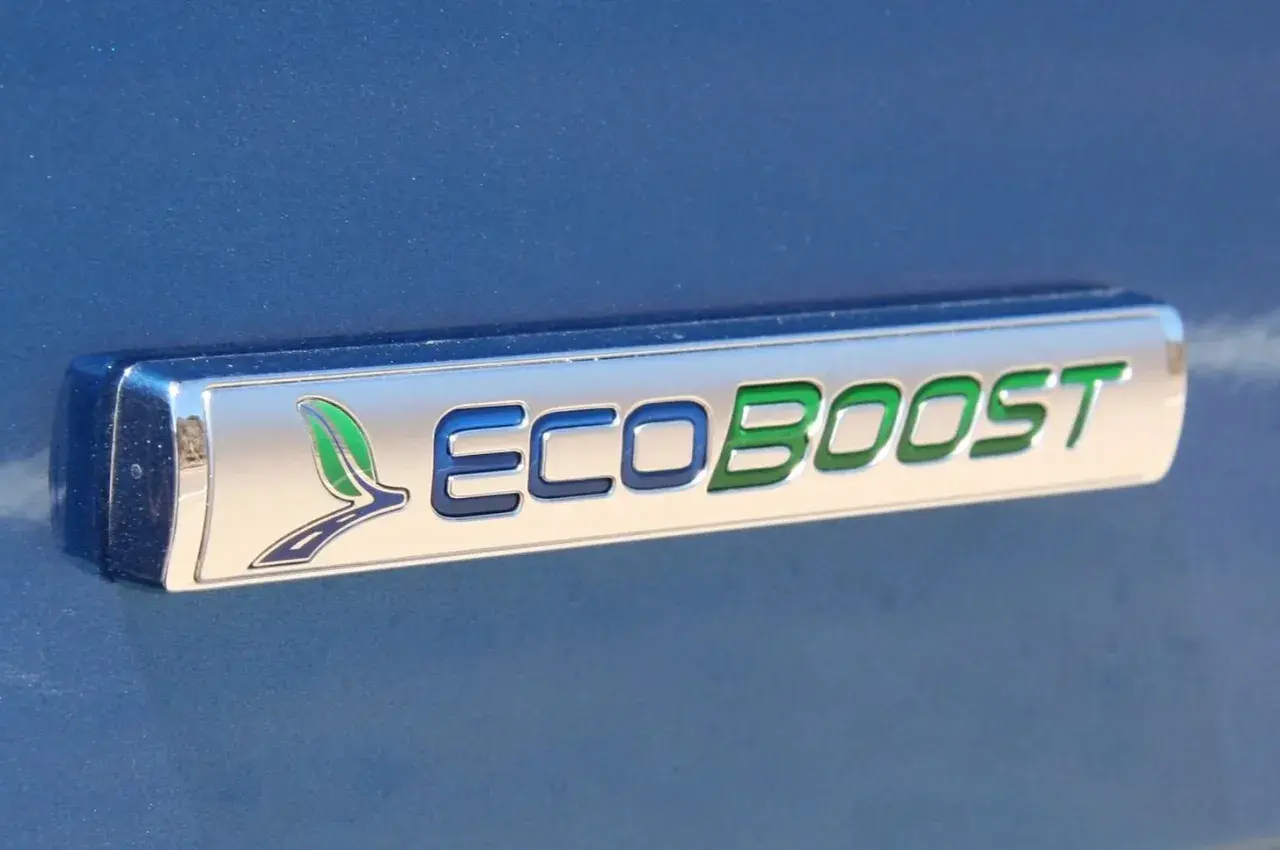 Ford Focus 1.0 EcoBoost kamremsbyte pris. Ett emblem på en blå bil visar "ECOBOOST" med gröna och blå bokstäver.