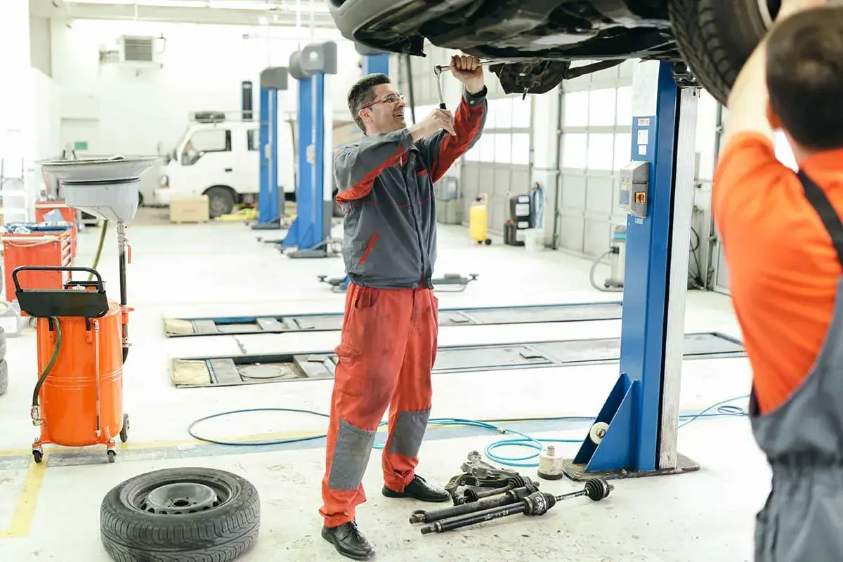 Mecánicos trabajando en el mantenimiento de coches en un taller. Uno usa una llave inglesa en el coche elevado, otro se prepara.