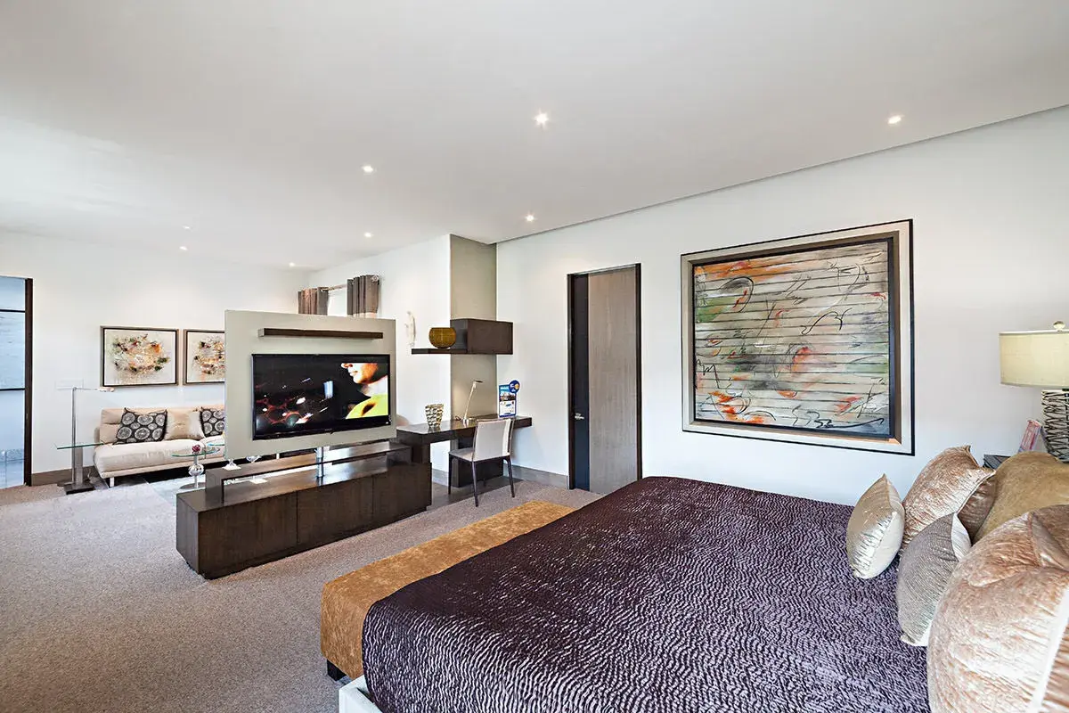 Modernes Schlafzimmer mit einem großen Fernseher im Wohnbereich, der durch eine Trennwand vom Bett abgetrennt ist.