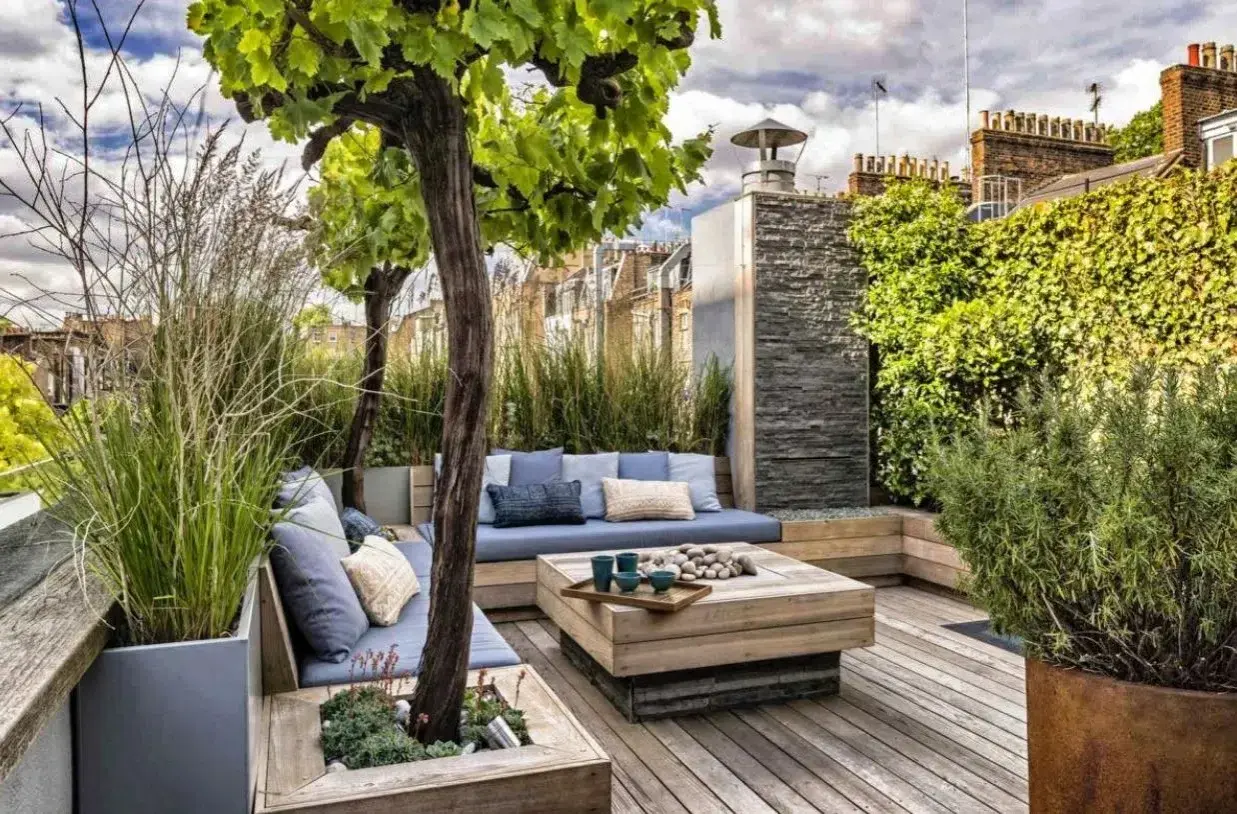 Aménagement autour d'une terrasse avec banquette bleue, table basse en bois et végétation luxuriante. Un espace détente chic et verdoyant.