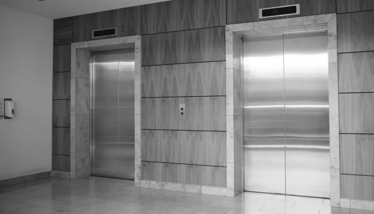 Dos ascensores modernos con puertas de acero inoxidable. Los ascensores tienen cámaras de seguridad integradas en el panel superior.