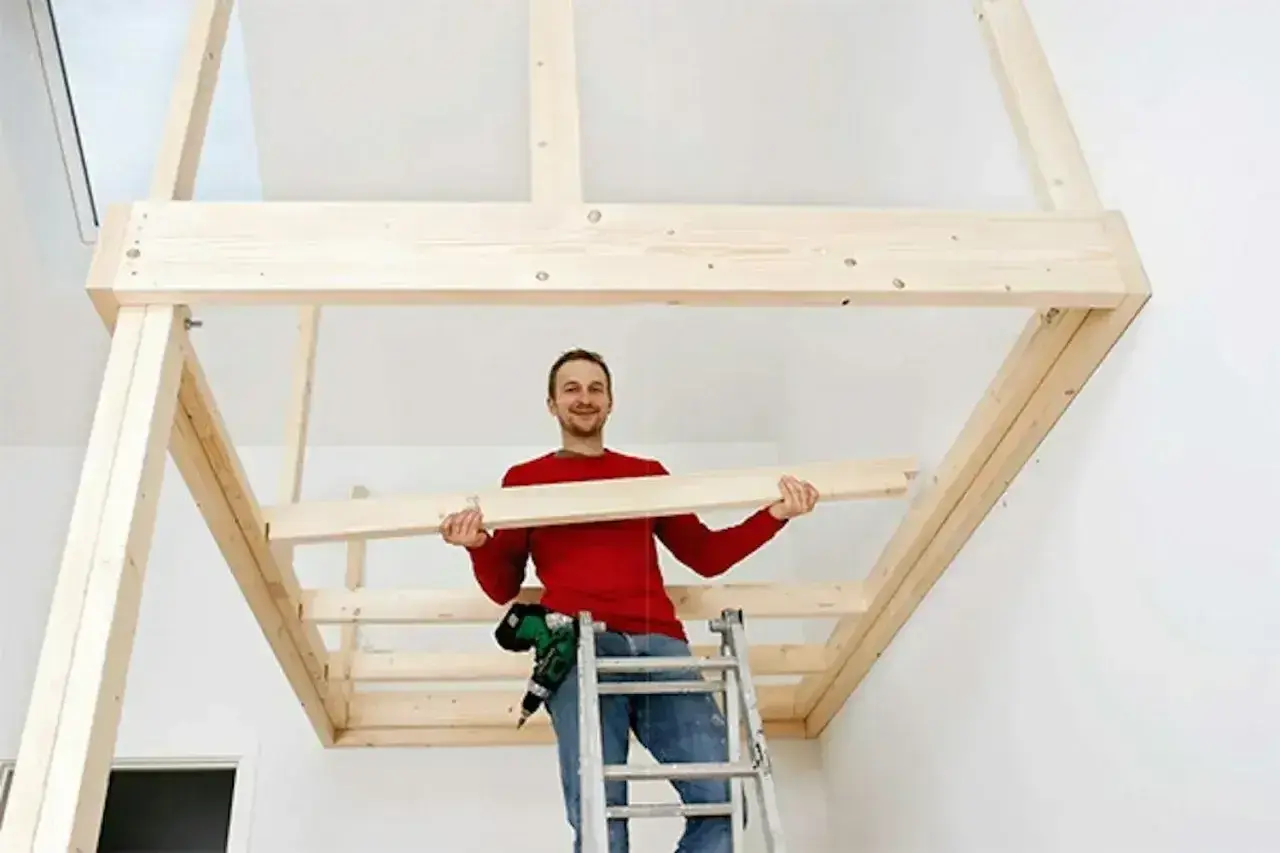 Man på en stege håller en träplanka, redo att bygga en stege till en loftsäng.