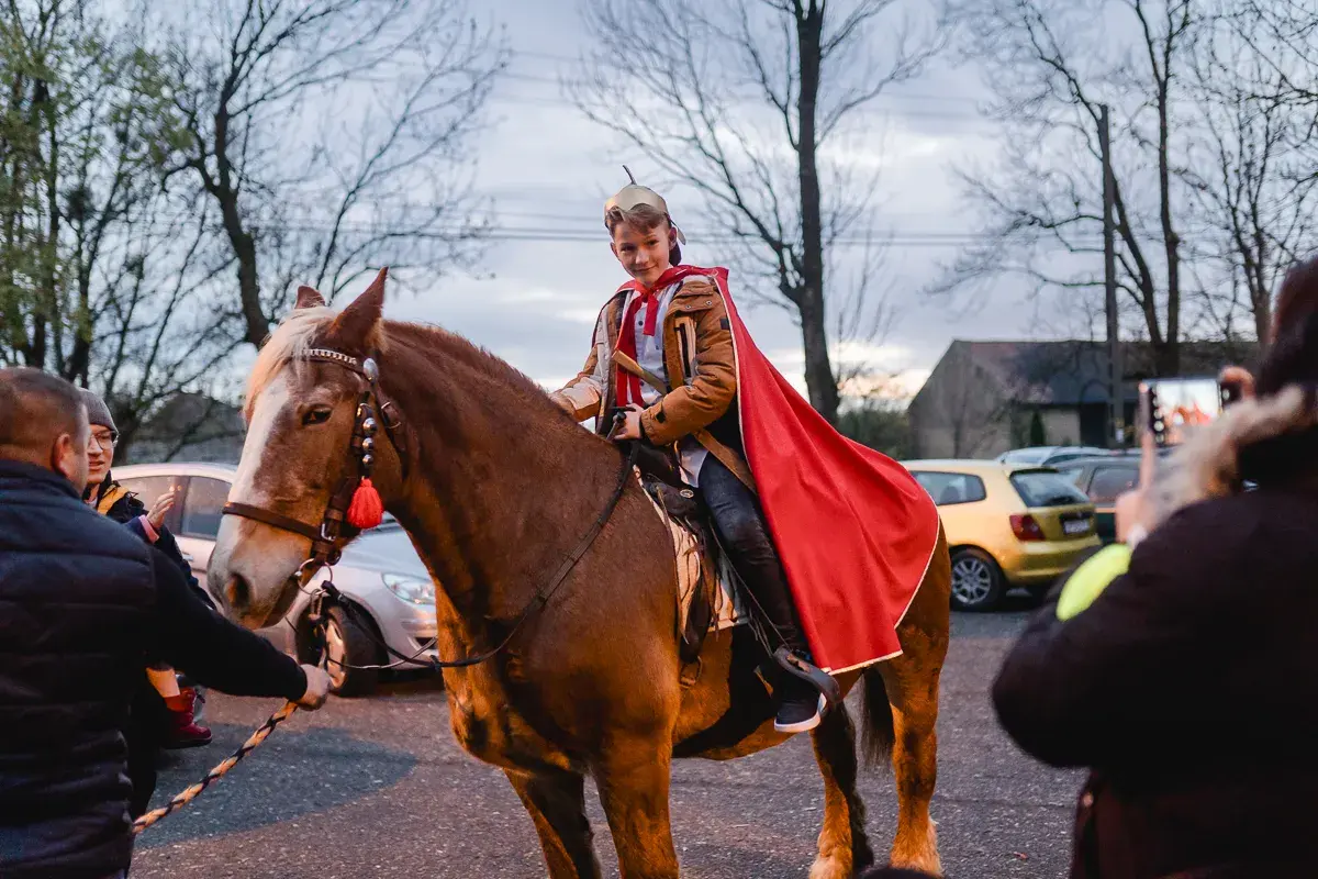 Chłopiec w stroju św. Marcina, na kasztanowym koniu, z czerwoną peleryną. To część tradycji bractwa konnego św. Marcina.
