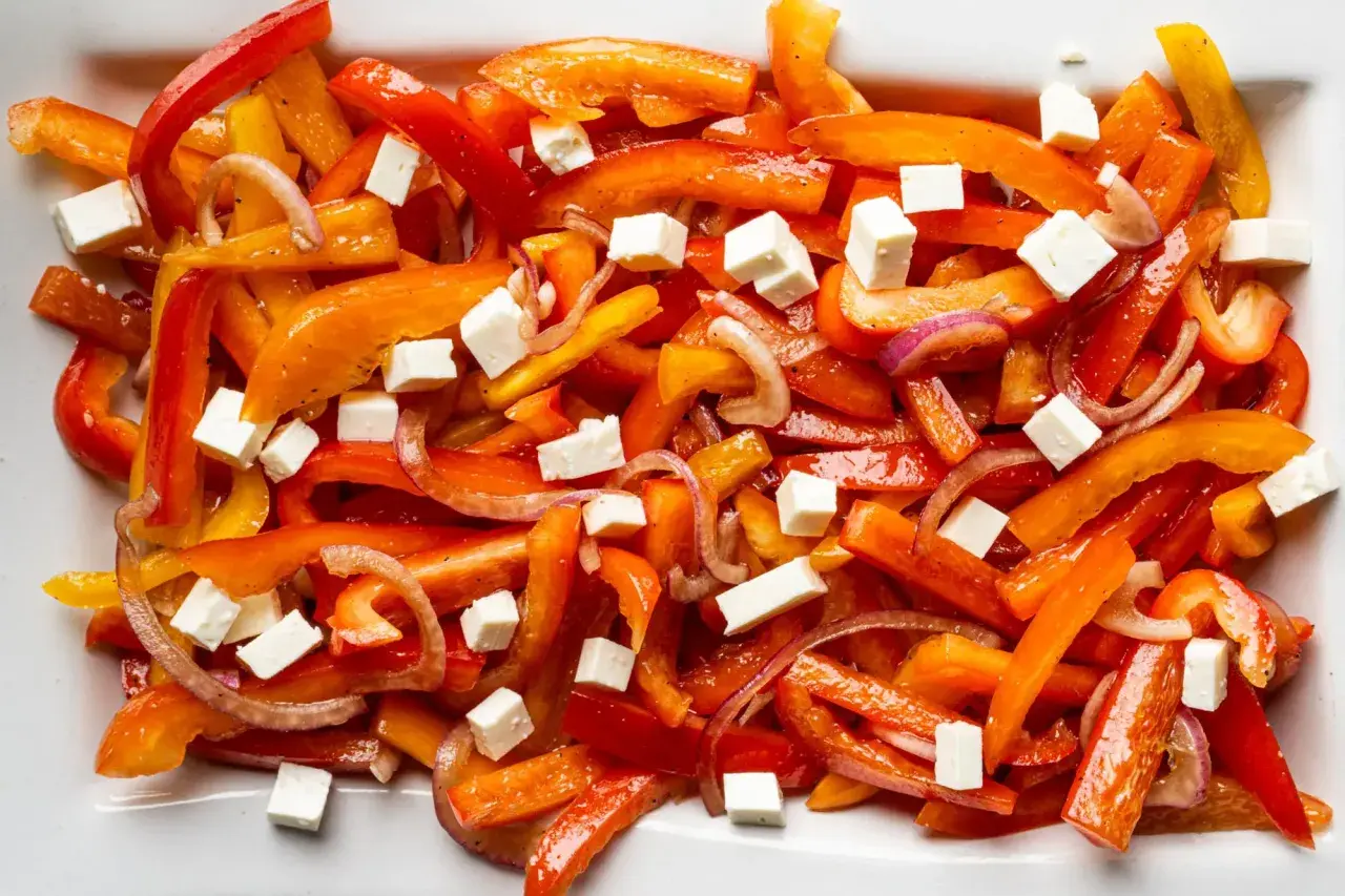 Bunter Paprika Salat mit roten Zwiebeln und weißen Würfeln, wahrscheinlich Feta-Käse.