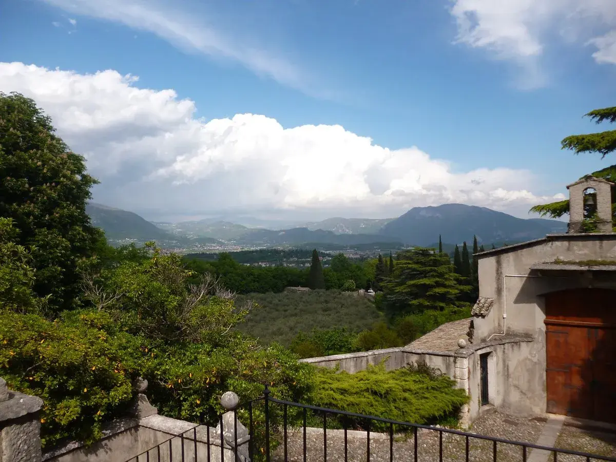 Panoramica sul percorso eremo dei camaldolesi Bardolino, con vista su colline, uliveti e montagne sotto un cielo nuvoloso.