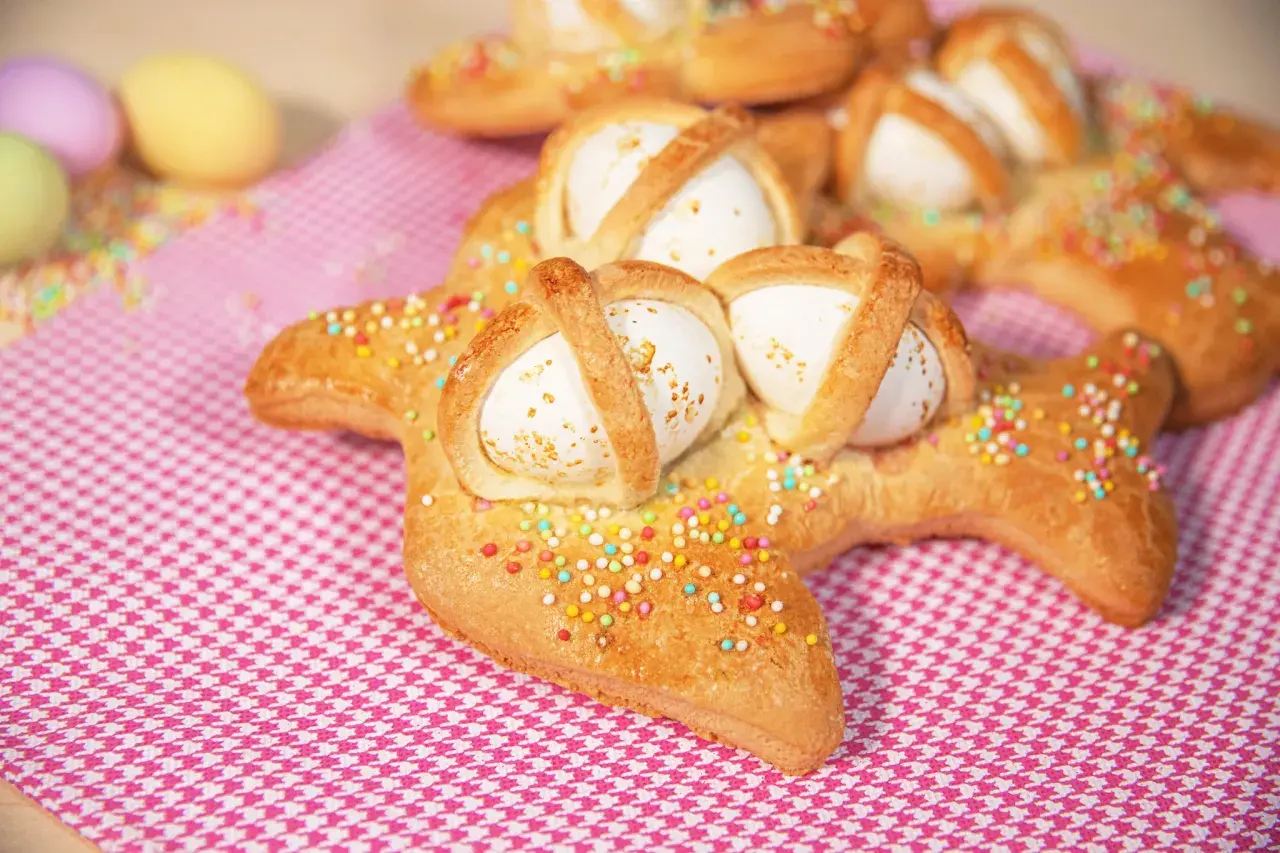 Scarcelle pugliesi ricetta originale: dolci a forma di colomba con uova sode, decorati con zuccherini colorati su tovaglia a quadretti rosa.