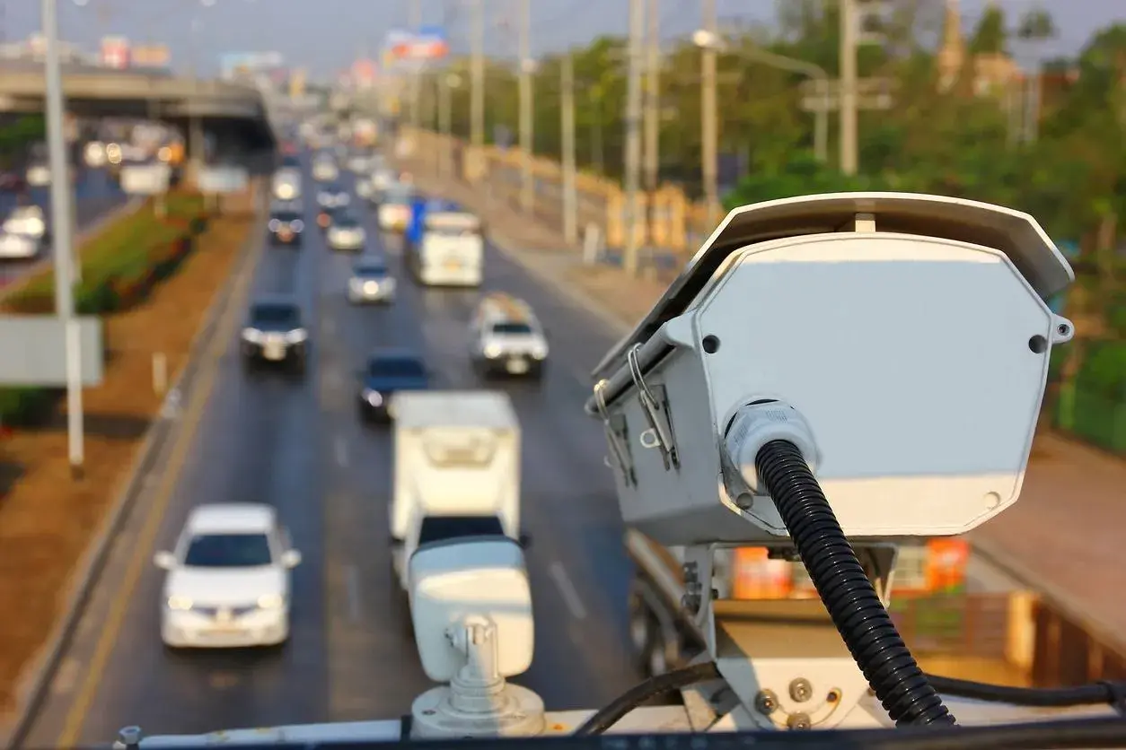Kamera monitorująca ruch drogowy. Czy policja może wykryć antyradar? Zbliżenie na białą kamerę z kablem, w tle ruchliwa autostrada.