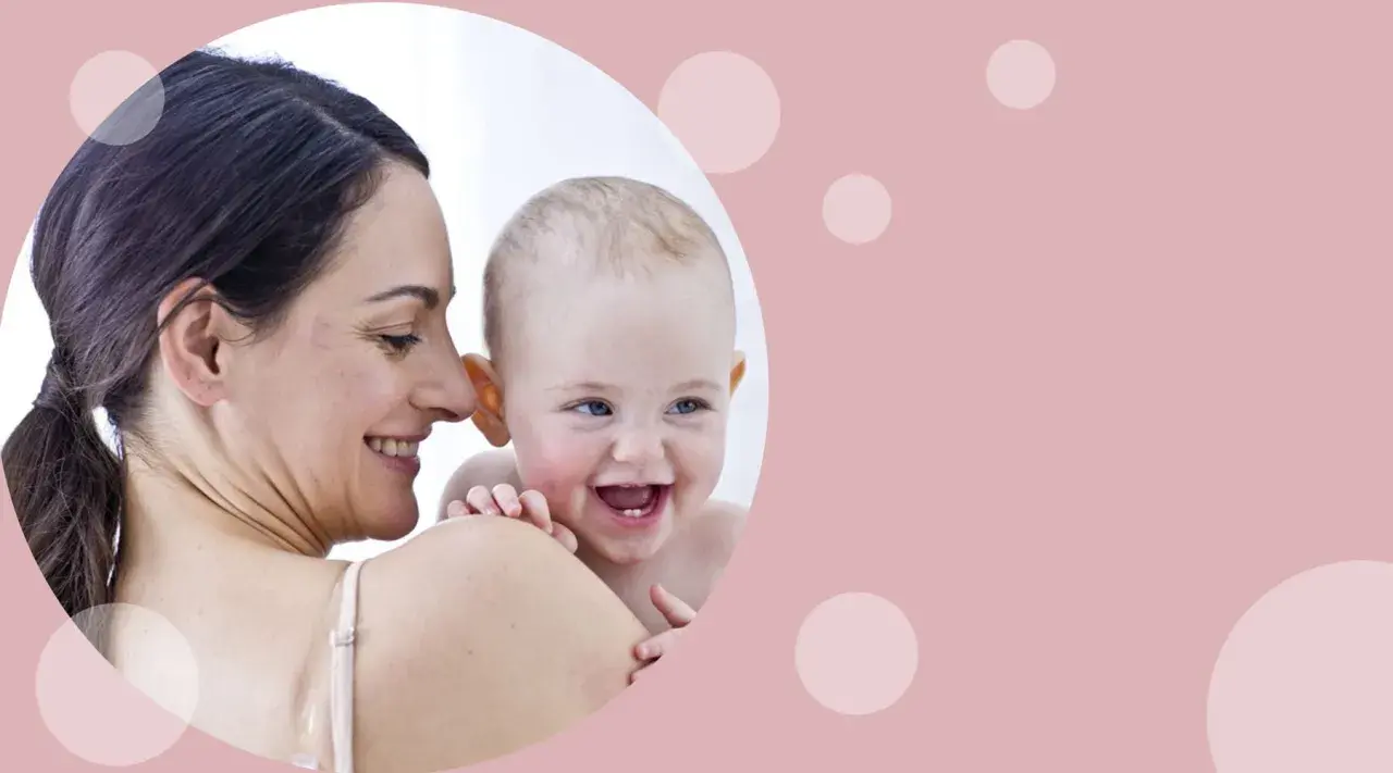 Uśmiechnięta mama tuli radosnego niemowlaka. Od kiedy oliwki dla niemowlaka? Pielęgnacja delikatnej skóry maluszka.