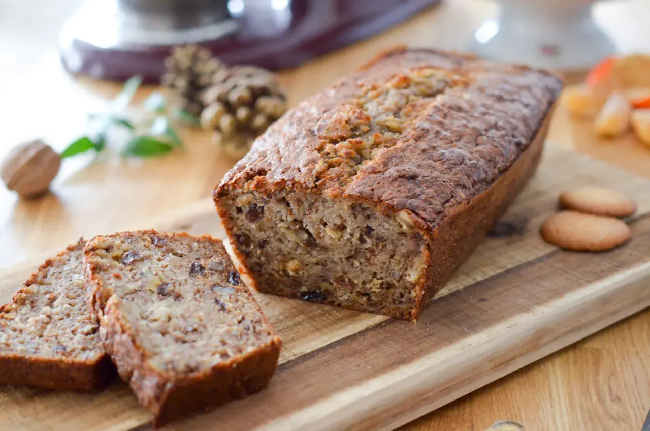 Un délicieux cake banane, coupé en tranches, sur une planche en bois. Des noix et des biscuits complètent cette gourmandise.