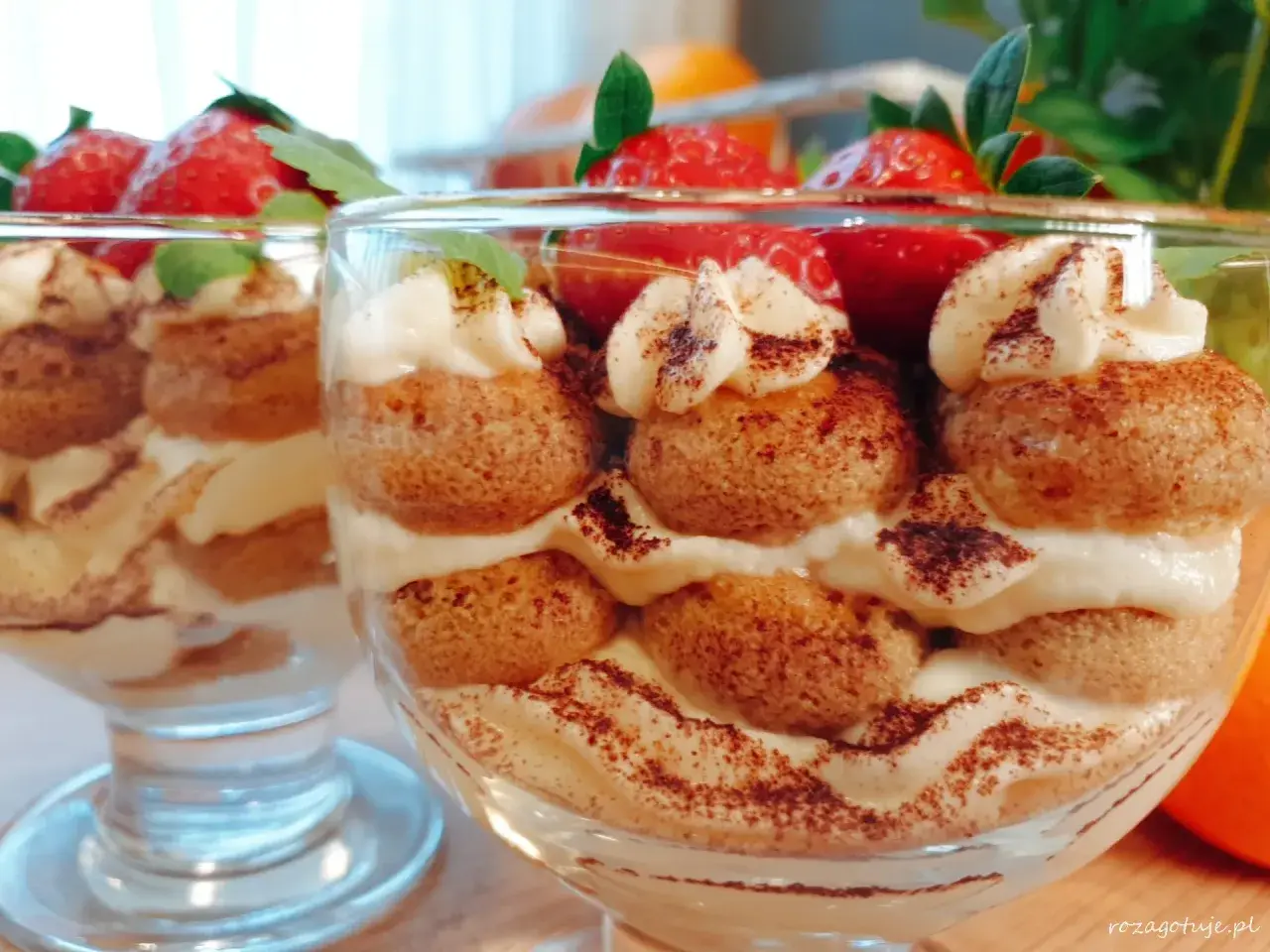 Pyszne tiramisu w pucharkach, przełożone kremem i biszkoptami, ozdobione truskawkami i kakao.