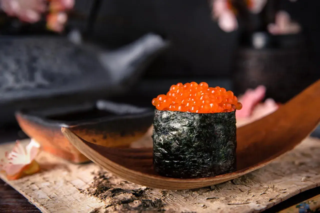 Wykwintny gunkan sushi z łososiem ikra, owinięty w ciemne nori, prezentowany na drewnianej łódce.