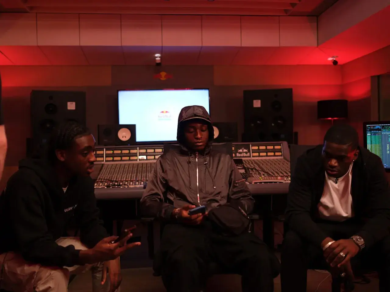 Trois jeunes hommes dans un studio d'enregistrement, discutant peut-être d'un cover rap gratuit.