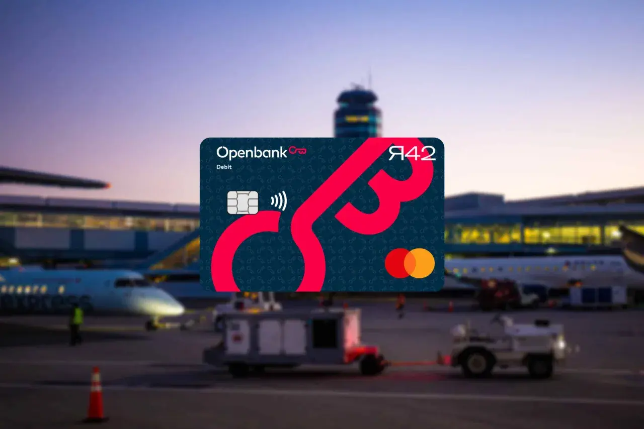 Openbank Debitkarte mit Mastercard-Logo vor einem Flughafen bei Dämmerung. Gute Openbank Erfahrungen für Reisen.