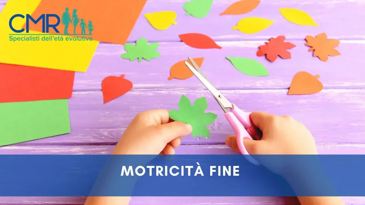 Mano di bambino che ritaglia forme di foglie colorate con forbici rosa, un'attività che stimola la motricità fine.