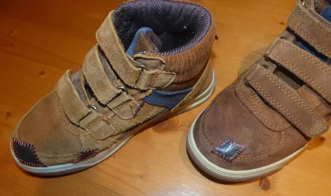 Paire de bottines marron avec des patchs noirs et roses sur le bout de chaussure abîmé.
